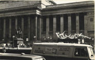 Large inflatable sculpture in front of civic building with a crowd of people and street traffic