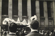 Large inflatable sculpture in front of civic building with a crowd of people and street traffic